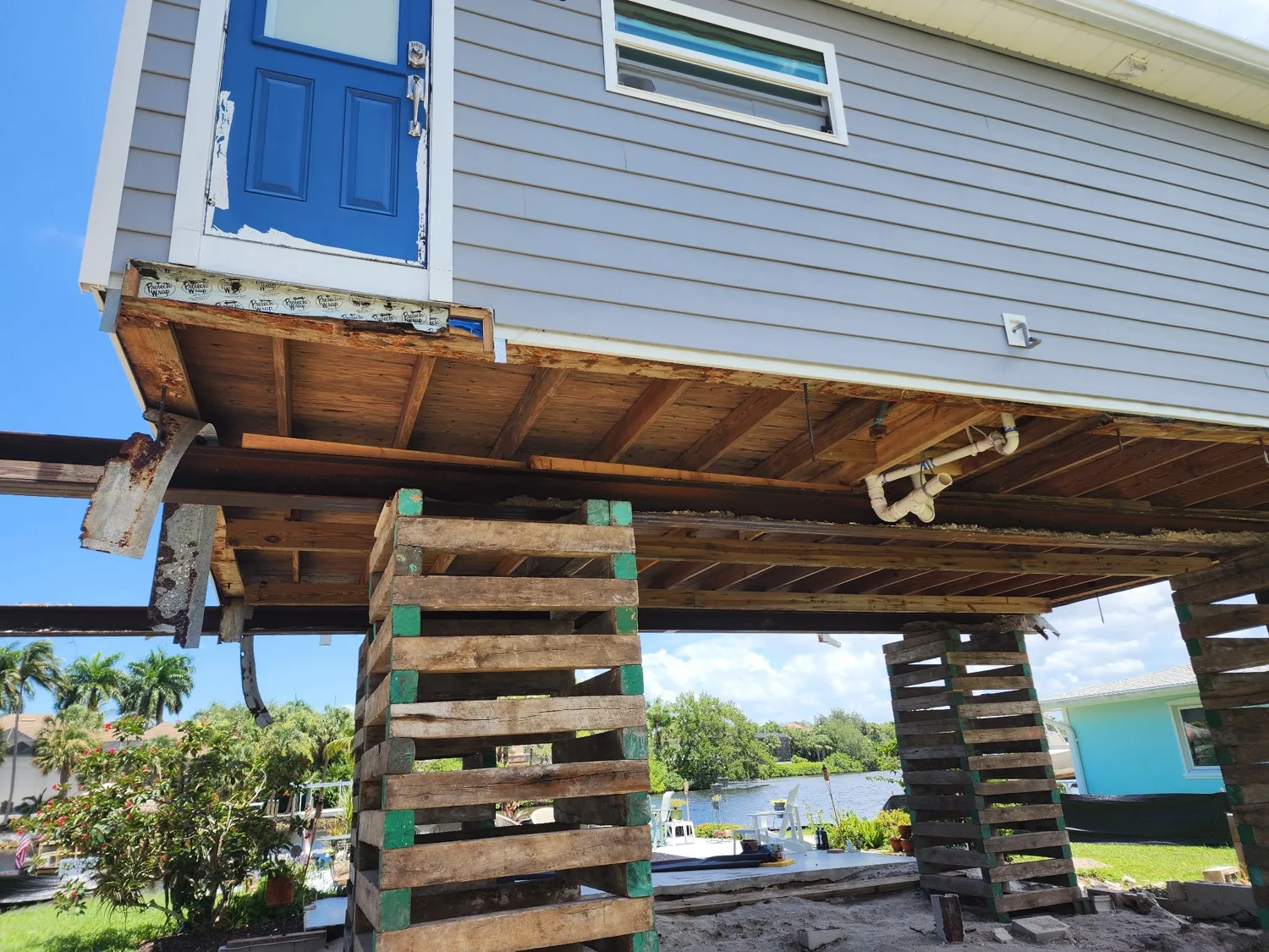 Side view of a waterfront home lifted clear of its original foundation on cribbing