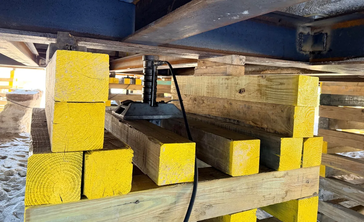 Close-up of hydraulic jack on yellow-painted wood cribbing beneath a home during a precision lift